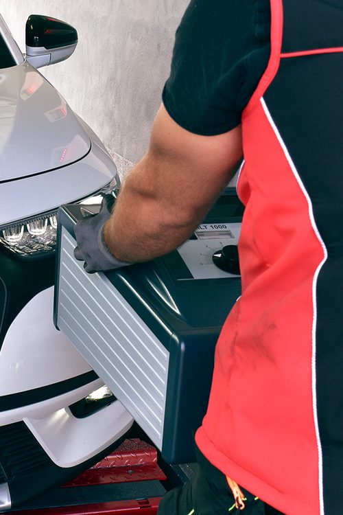 Prüfingenieur des Ingenieurbüros Wolk kontrolliert mit einem Prüfgerät die Frontbeleuchtung eines Fahrzeugs
