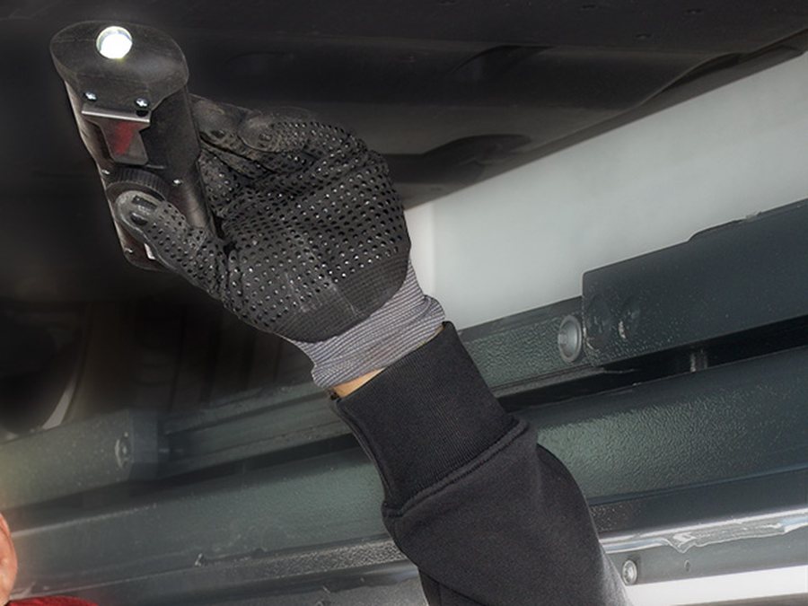 Prüfhand mit Handleuchte kontrolliert sicherheitsrelevante Bauteile am Unterboden eines angehobenen Fahrzeugs
